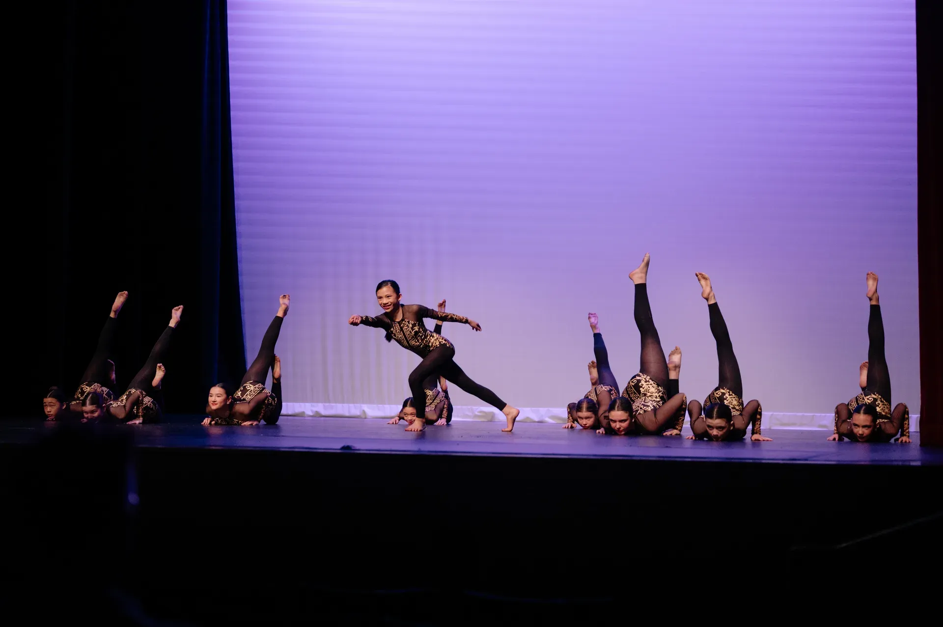 VPS acro dancers performing on stage under purple lights, legs raised in synchronized formation