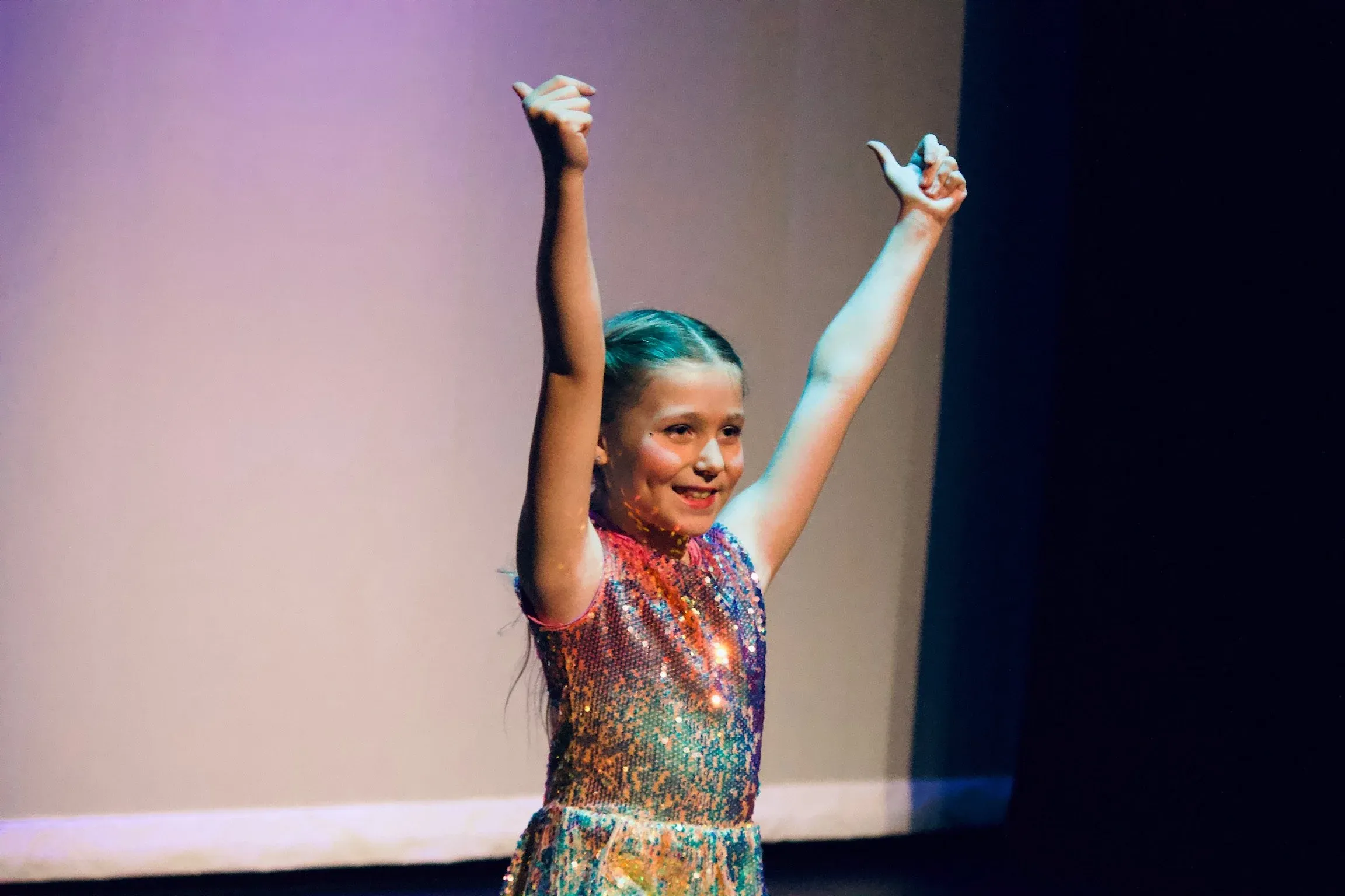 Young VPS student in sequin costume performing on stage with arms raised