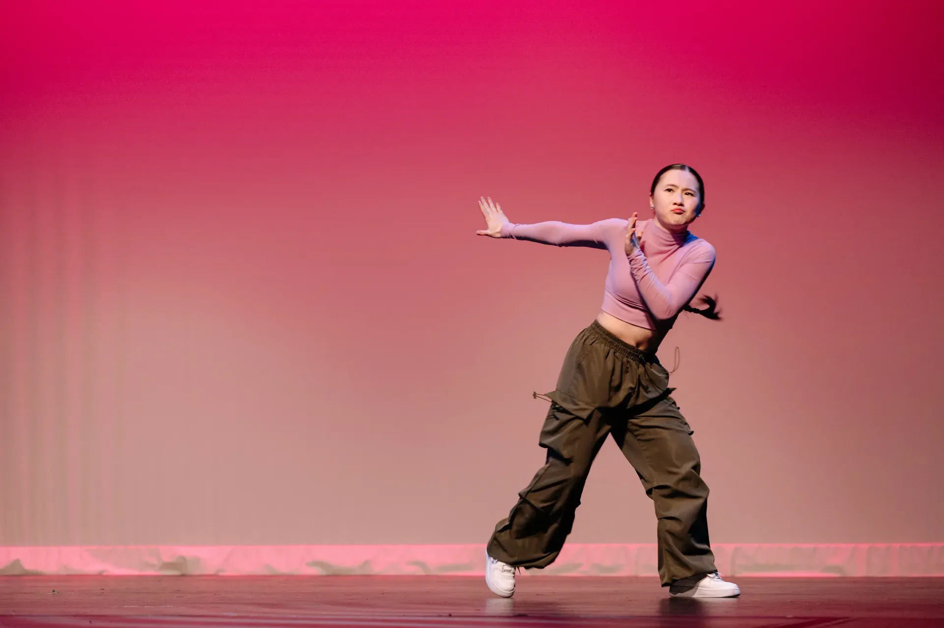 VPS hip hop dancer performing on stage against a pink background, cargo pants and sharp arm movements