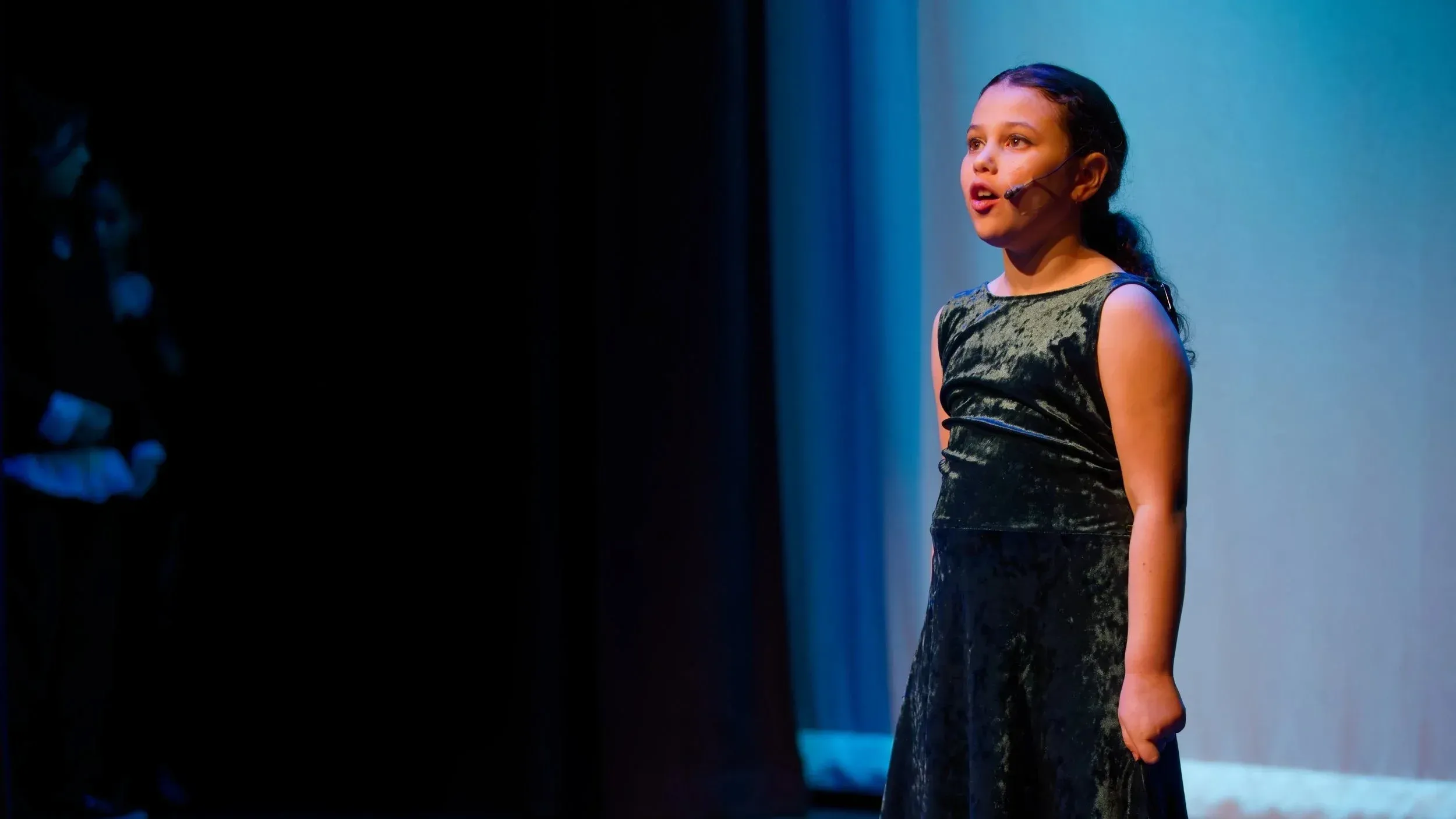 VPS soloist performing on stage in a velvet dress, lit by blue stage lighting