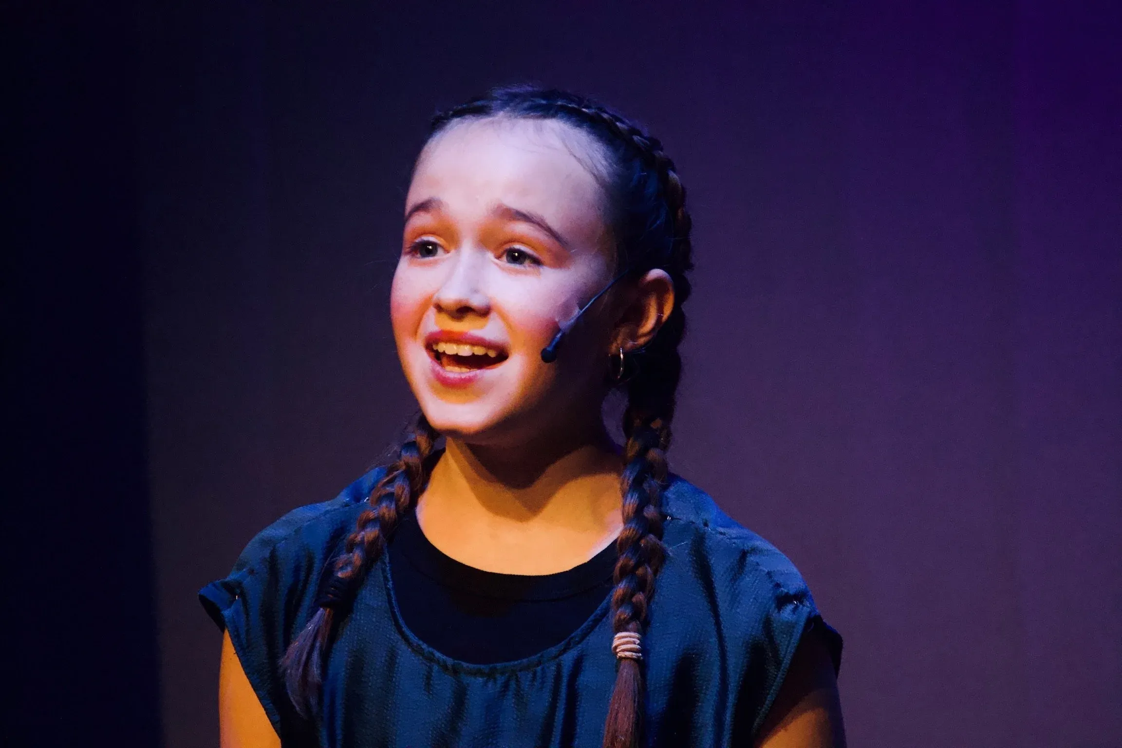 Young VPS vocalist performing on stage with a headset mic, lit by purple stage lighting