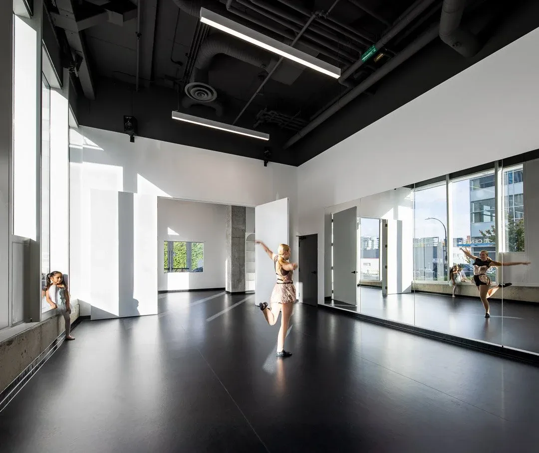 Young dancer mid-pose in the VPS dance studio in Mount Pleasant, with black floors, mirrors, and natural light