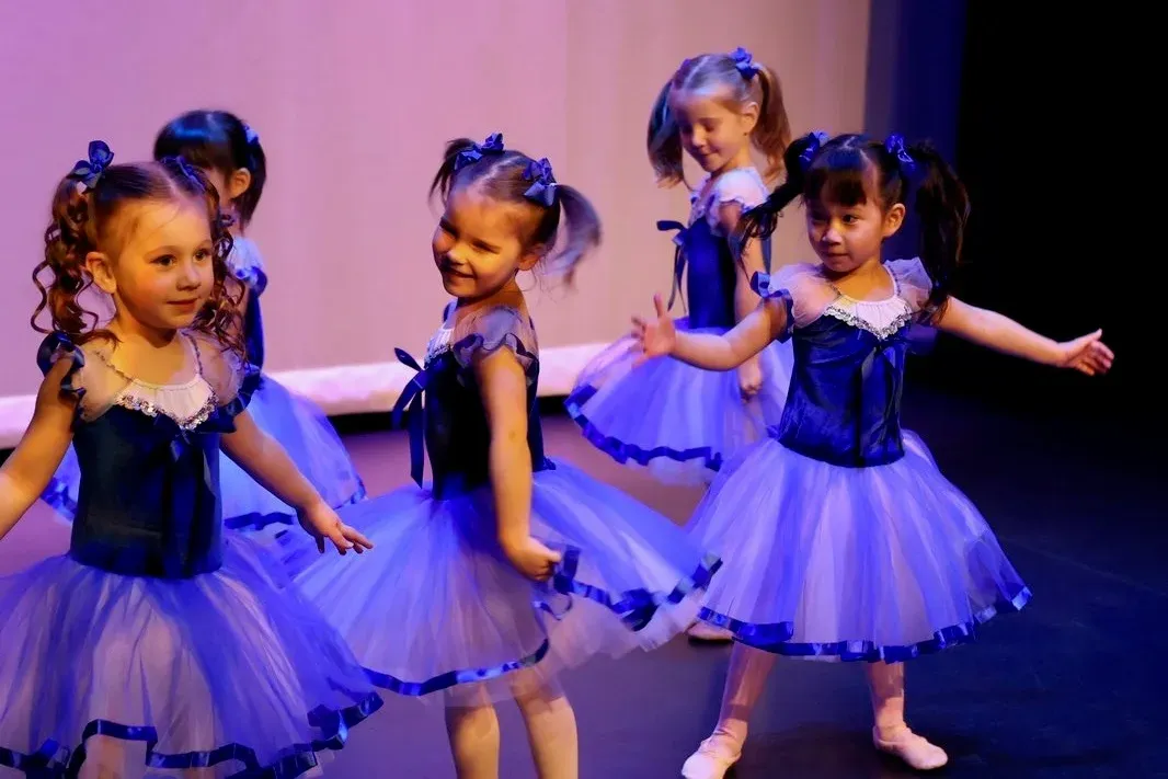 Young VPS ballet dancers performing on stage in blue tutus, smiling and twirling